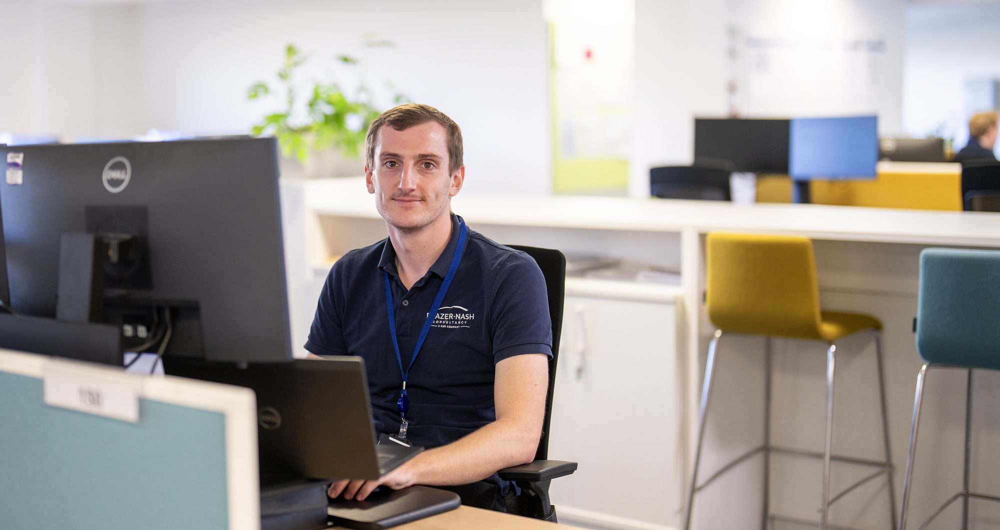 A Frazer-Nash employee at his desk, wearing a Frazer-Nash lanyard